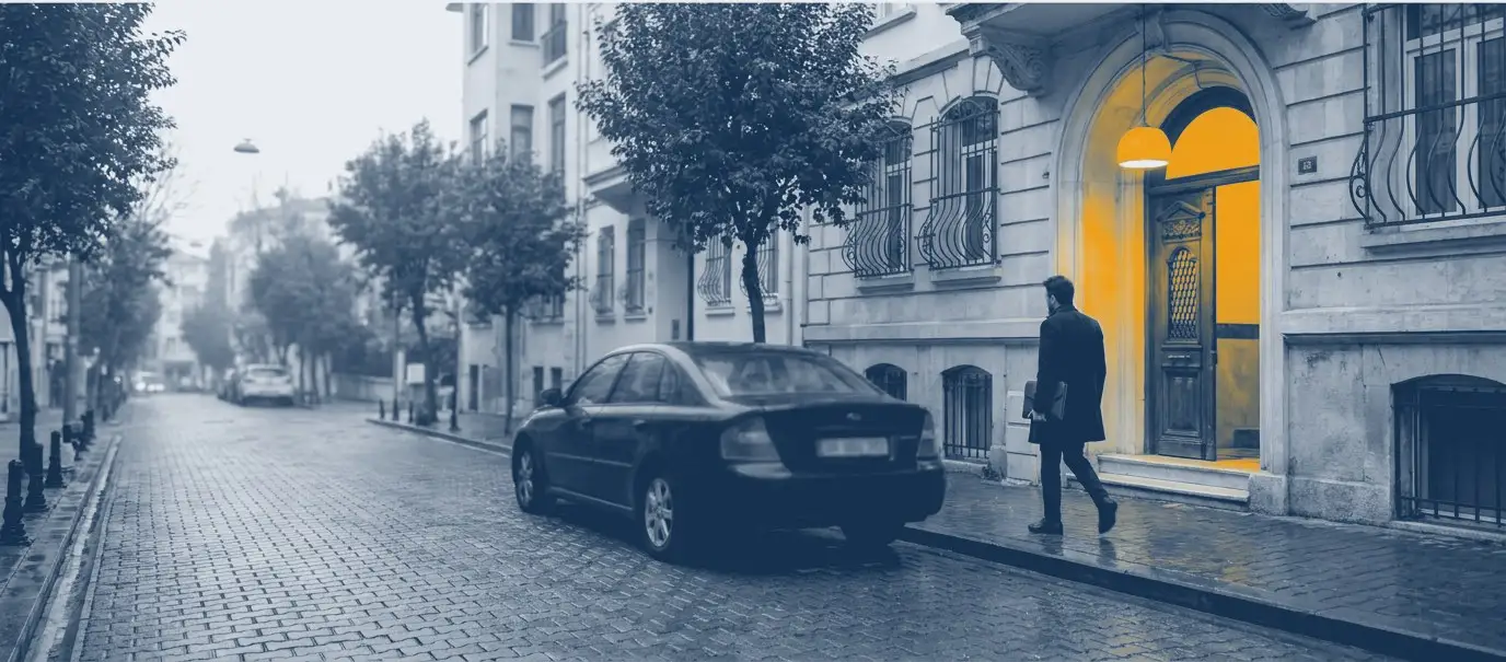 Sisli, ıslak taş döşeli bir İstanbul sokağında park etmiş araç ve amber ışıklı bir kapıya yürüyen figür